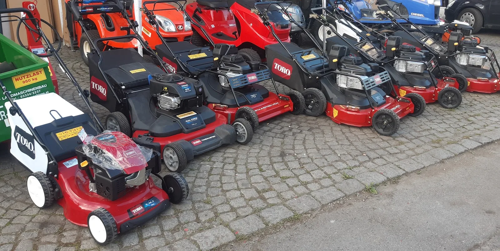 Reihe roter TORO Rasenmäher auf dem gepflasterten Platz vor dem Geschäft